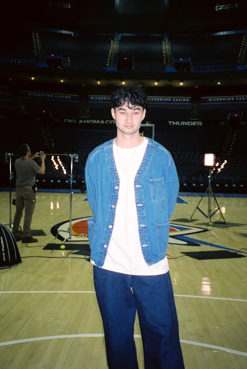 Ken Dowling in a denim jacket, standing courtside at a basketball arena.